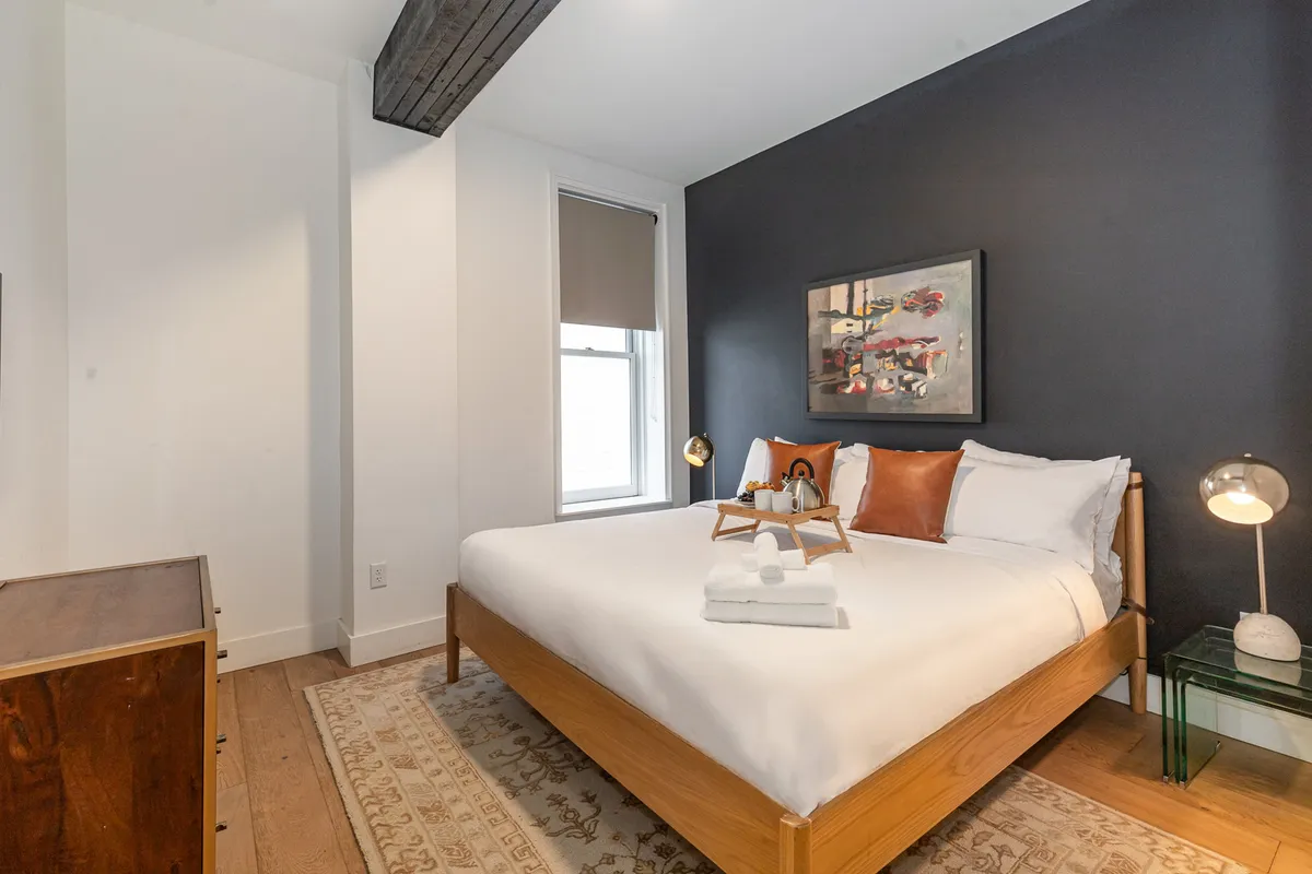 A secondary bedroom with a neatly made bed, artistic wall decor, and a nightstand, bathed in natural light. The overall atmosphere is calm and tranquil, geared toward relaxation and quiet moments.