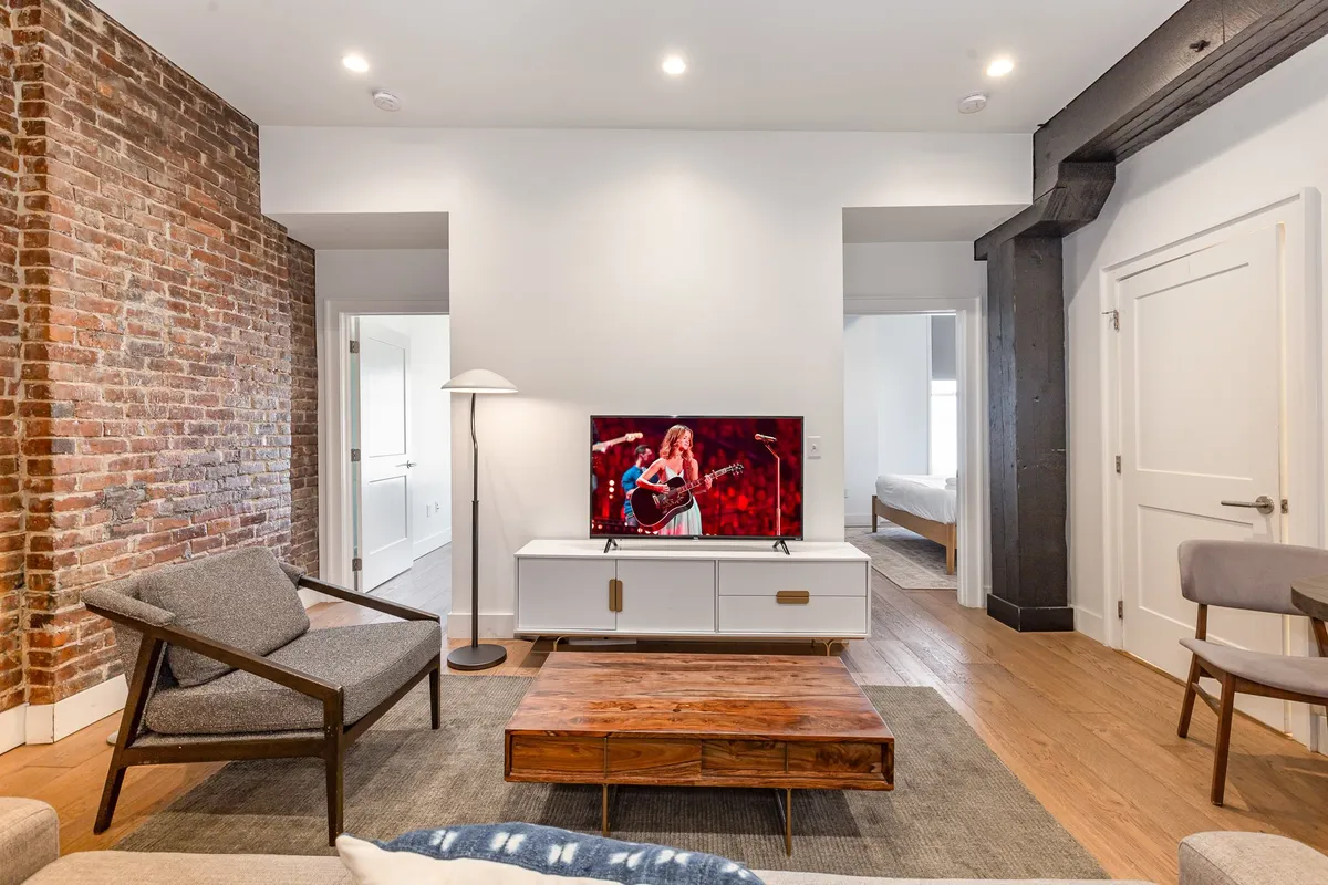 A casual, inviting living room with a brick wall backdrop, television, coffee table, and plush sofa. The arrangement is great for watching TV, playing games, or just relaxing together, offering a cozy yet energetic atmosphere.