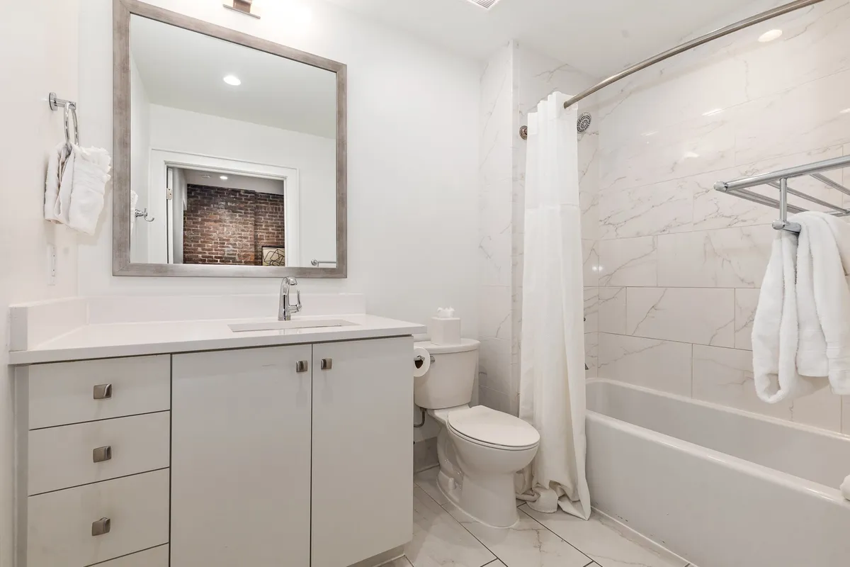 A contemporary full bathroom featuring a large mirror, a vanity with sink, a bathtub, toilet, and a towel rack. The design is clean, minimalist, and functional—suited for both quick refreshes and longer, restorative soaks.
