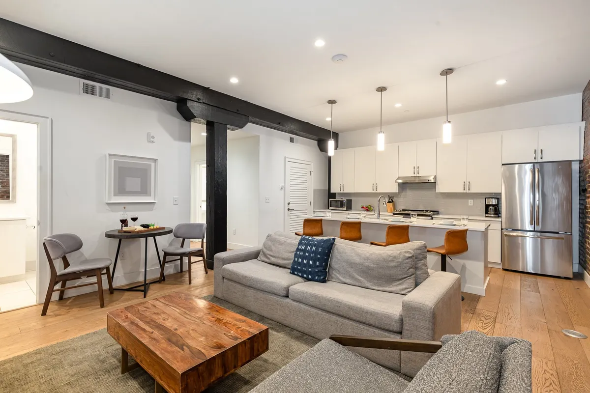 The image features a warm, inviting living space with a plush sofa, a rustic wooden coffee table, and a sleek kitchen island in view. The layout encourages socializing, whether guests are lounging, sharing drinks, or preparing meals together. The ambiance is cozy and modern, perfect for gathering with friends or family after exploring downtown Nashville.
